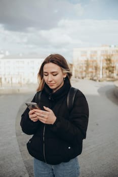 gorgeous beautiful young woman with blonde hair messaging on the smart-phone at the city street background. pretty girl having smart phone conversation in sun flare.