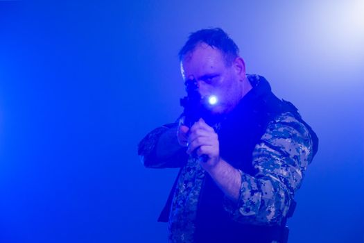 Soldier in army fatigues holding assault rifle in haze of blue smoke