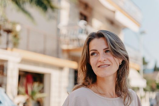 Girl tourist walking through ancient narrow street on a beautiful summer day in MEDITERRANEAN MEDIEVAL CITY , OLD TOWN bUDVA, MONTENEGRO. Young beautiful cheerful woman walking on old street at tropical town. Pretty girl looking at you and smiling