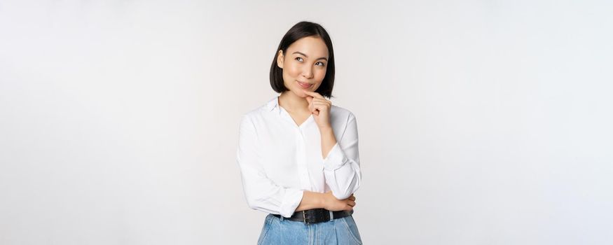 Image of thoughtful smiling woman has an idea, scheming, planning, looking aside and thinking, standing in office white blouse against studio background.