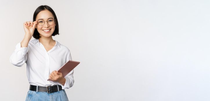 Image of young asian business woman, female entrepreneur in glasses, holding tablet and looking professional in glasses, white background.