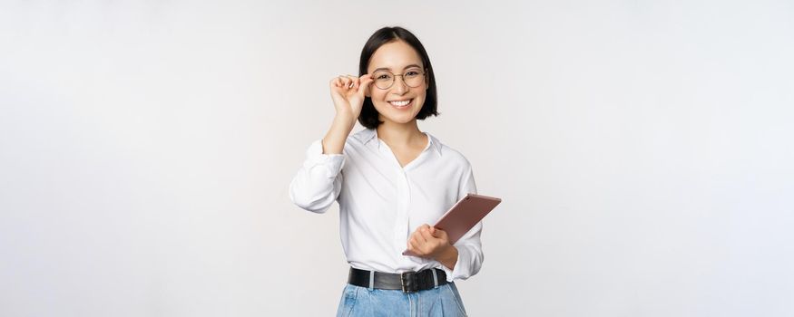 Image of young asian business woman, female entrepreneur in glasses, holding tablet and looking professional in glasses, white background.