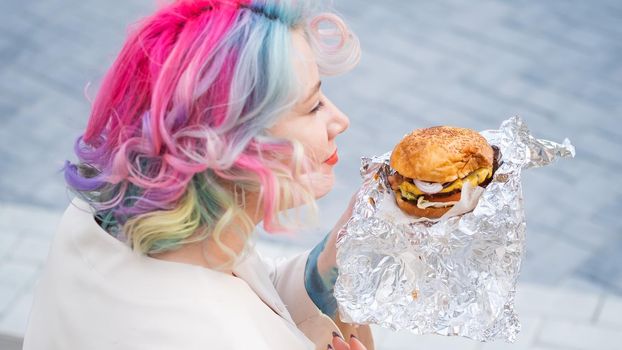 Caucasian woman with curly colored hair eating burger. Bad eating habits and love of fast food.