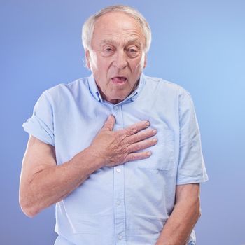 Studio shot of a senior man experiencing chest discomfort against a blue background.