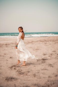 Model in boho style in a white long dress and silver jewelry on the beach. Her hair is braided, and there are many bracelets on her arms