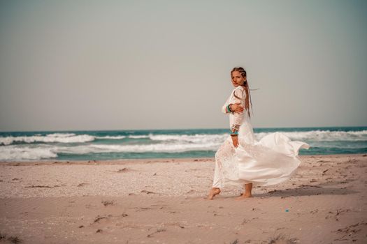 Model in boho style in a white long dress and silver jewelry on the beach. Her hair is braided, and there are many bracelets on her arms