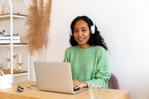 African-american woman typing on laptop while listening to audio podcast in earphones. Concept of distance studying and working. Millennial taking online courses. Leisure entertainment activity