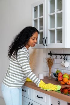 African-american femal dust handling with washcloth. Concept of cleaning kitchen and doing chores around house. Sweeping kitchenette unit after cooking. Removing dirt from surface. Vertical