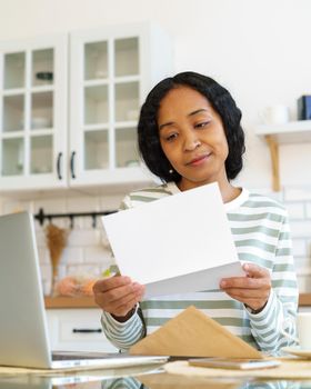 African-american woman smiling while reading paper letter. Concept of receiving correspondence. Opening envelope with documents. Vertical of postage hobby. Looking for news with interest