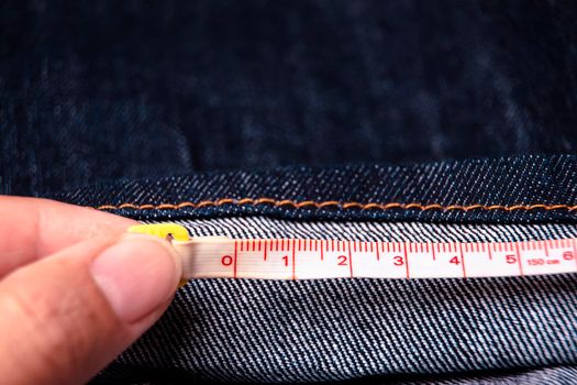 Hand of tailor measure the length of the jeans with a measuring tape