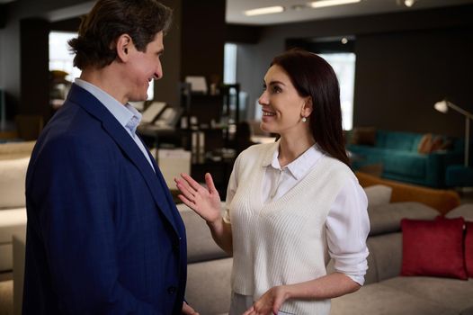 Pretty woman buying upholstered furniture in a furniture store, listening to the recommendations of the sales manager in the showroom