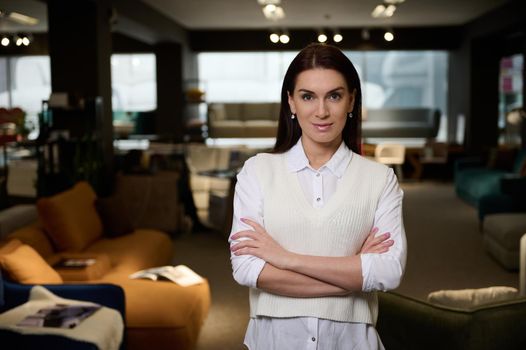 Beautiful successful business woman, confident female sales manager of a furniture store looking at camera smiling with arms crossed