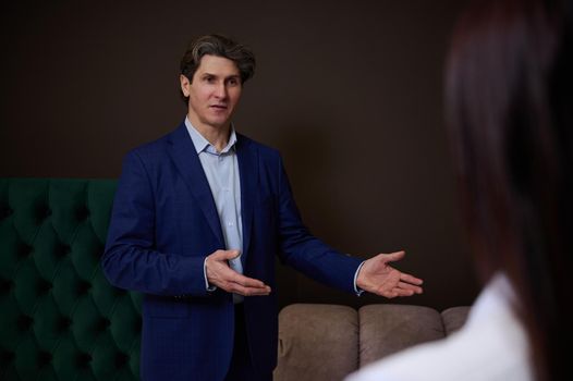 Confident sales rep, retail manager, assistant in upholstered furniture store showroom presents orthopedic mattresses to female customer, helping her to make purchase for home improvement