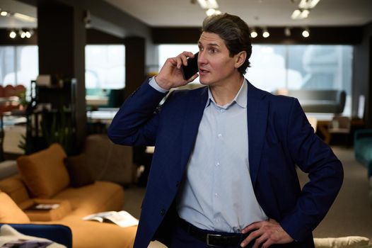 Portrait of a confident businessman, entrepreneur, successful sales manager, retail assistant, interior designer talking on mobile phone while visiting a furniture store showroom