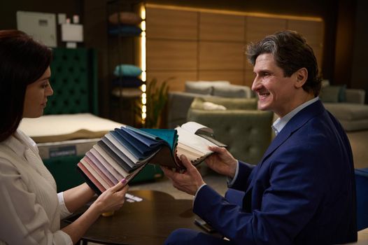 Rear view of a middle aged Caucasian couple holding color fabric samples and picking couch seat cover in the furniture store.