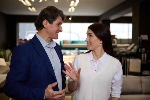 Happy middle aged Caucasian couple make purchases in an exhibition center of upholstered furniture. Beautiful woman and handsome man, husband and wife buying sofa in the showroom. Home interior design