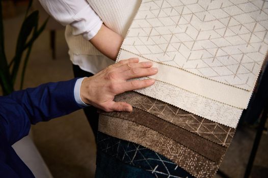 Close-up. Interior designer points to the fabric that he likes, choosing the fabric in the catalog with fabric samples for new sofa.