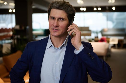 Portrait of a confident businessman, entrepreneur, sales manager, retail assistant, interior designer talking on mobile phone while visiting a furniture store exhibition hall