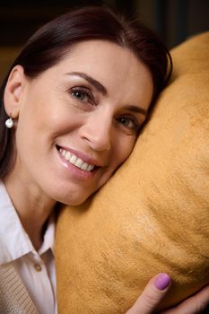 Headshot. Delightful beautiful relaxed serene middle-aged Caucasian woman smiles looking at camera while leaning her head on a velour cushion. Healthy pleasant sleep and home interior design concept