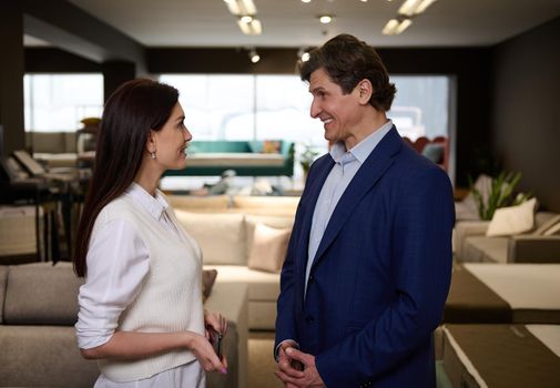 Handsome Caucasian man buying upholstered furniture in a furniture store, listening to the recommendations of the sales manager in the showroom