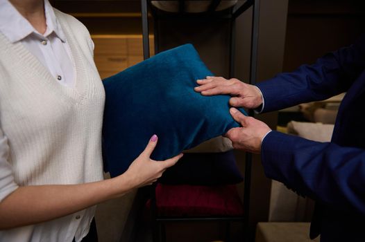 Close-up of customers hands touching a pillow standing near a stand with cushions in the furniture store