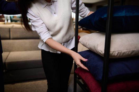 Close-up of an elegant European woman selecting new sofa pillow and cushion on the expo stand in the exhibition center of a furniture store. Home improvement, home comfort and interior design