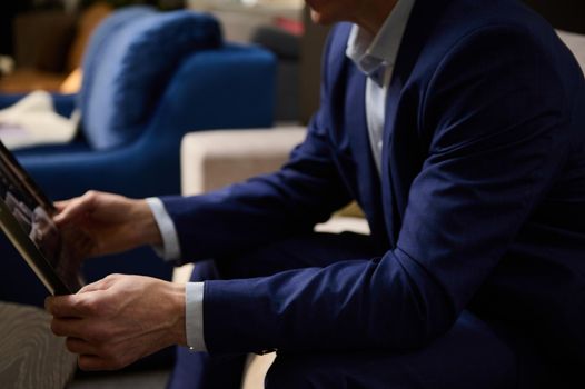 Cropped image. Hands of a man in business suit holding a catalog and sitting on a sofa in the showroom of an upholstered furniture store. Small, business, interior design, home improvement concept