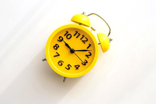 A yellow retro alarm clock with a black dial lies on a white table diagonally to the left. view from above. copy space