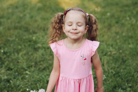 A little cute baby girl in a pink dress in a green park in spring or summer