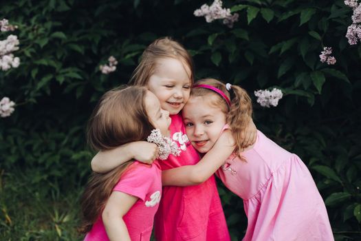Three beautiful cute girls and girlfriends hug in pink dresses in a blooming park in spring