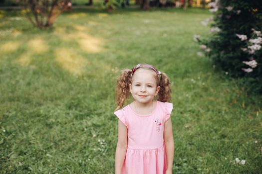 A little cute baby girl in a pink dress in a green park in spring or summer