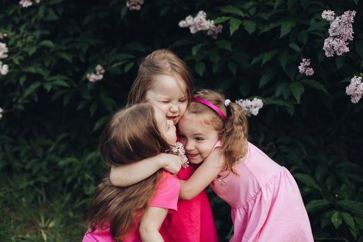 Three beautiful cute girls and girlfriends hug in pink dresses in a blooming park in spring