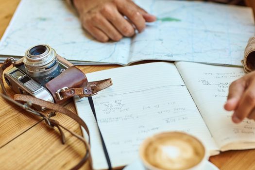 Shot of an unidentifiable tourist looking at maps and travel journals while enjoying coffee at a cafe.