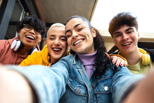 Smiling multiracial group of friends take selfie with phone outside university building. Students laughing and having fun. Youth lifestyle and social media concept.