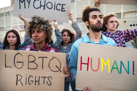 Multiracial group of people march together protesting on a demonstration for LGBT rights holding cardboard banners. Activist concept.