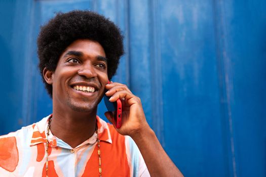 Smiling, happy African American man using mobile phone to talk. Black male with afro hairstyle on a phone call in the street. Lifestyle and technology concept.