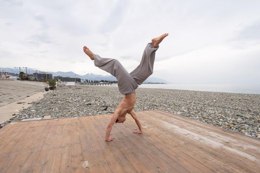 Shirtless caucasian man doing backflip on pebble beach