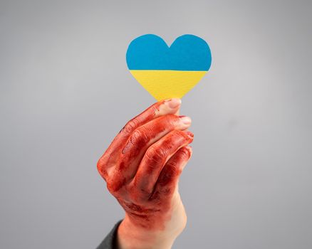 Woman with hands covered in blood holding a heart with the flag of ukraine on a white background