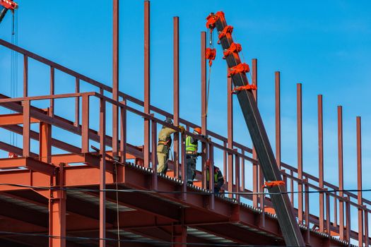 Builders fix iron beams with a crane. Frame construction.