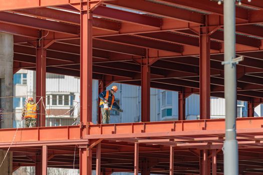 A male builder works with a hand tool on a frame of iron beams. Construction. Moscow Russia April 14, 2022