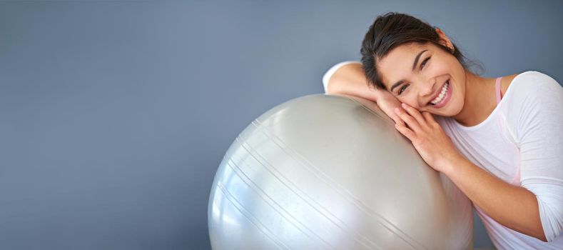Cropped shot of a sporty young woman leaning on a pilates ball against a grey background.