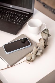 White desktop with laptop, coffee mug, phone and notebook for remote work or study. Office computer workplace in home interior.