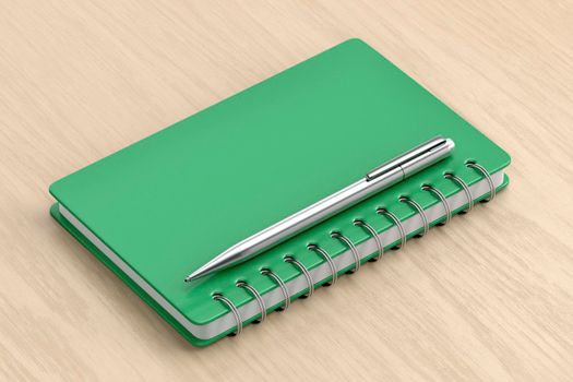 Green spiral notebook and silver pen on wooden table