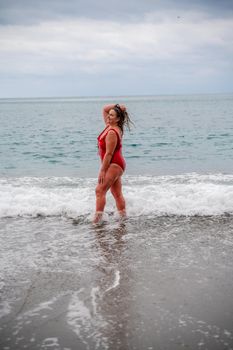 Woman in a bathing suit at the sea. A fat young woman in a red swimsuit enters the water during the surf.