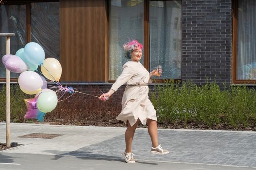 Woman in colored hair walks with an armful of balloons and drinks a refreshing beverage.