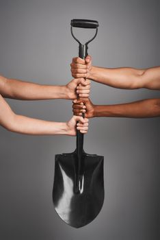 Studio shot of unidentifiable hands holding on to a shovel against a gray background.