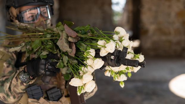 Caucasian woman in military uniform holding a machine gun and a bouquet of white roses