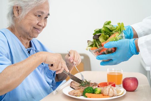 Asian senior or elderly old lady woman patient eating breakfast and vegetable healthy food with hope and happy while sitting and hungry on bed in hospital.