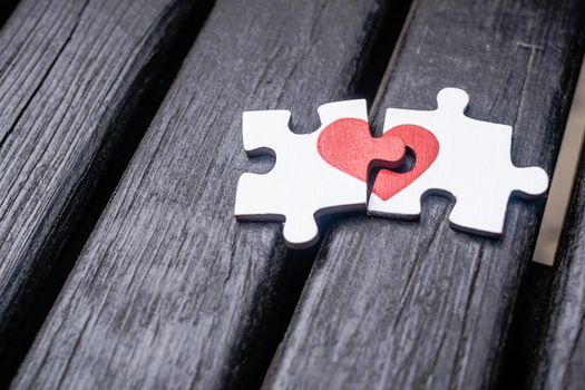 Red heart is drawn on the pieces of the wooden puzzle lying next to each other on wooden background. Love concept.