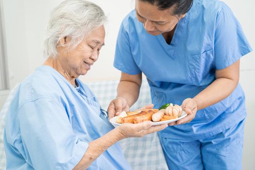 Asian senior or elderly old lady woman patient eating breakfast and vegetable healthy food with hope and happy while sitting and hungry on bed in hospital.